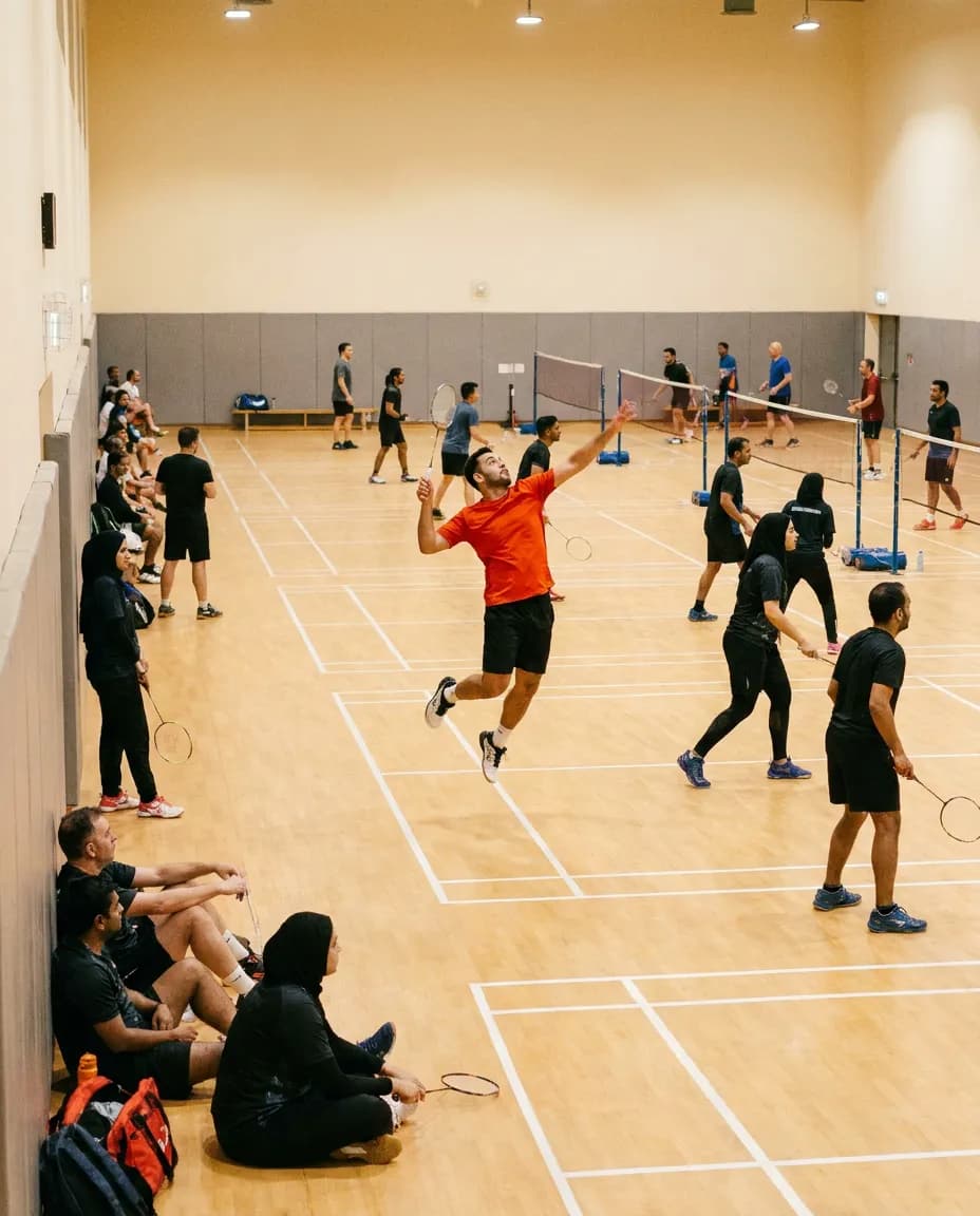 A player mid-smash at an evening community badminton session in a sports hall